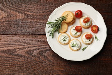 Tasty crackers with cream cheese, rosemary and tomatoes on wooden table, top view. Space for text
