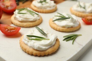 Tasty crackers with cream cheese, rosemary and tomatoes on white table, closeup