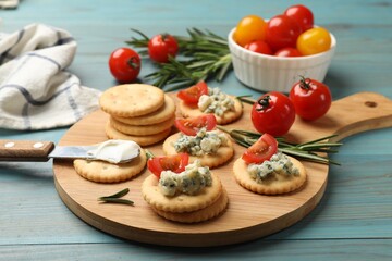 Tasty crackers with blue cheese, rosemary and tomatoes on wooden table, closeup