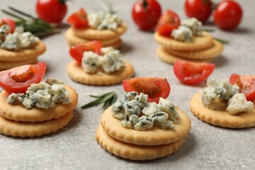 Tasty crackers with blue cheese, rosemary and tomatoes on grey textured table, closeup