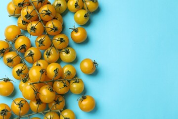Ripe yellow cherry tomatoes on light blue background, flat lay. Space for text