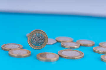 This is a close-up shot of British one-pound coins scattered across a bright blue surface. The coins feature the Scottish thistle symbol on the one-pound coin.