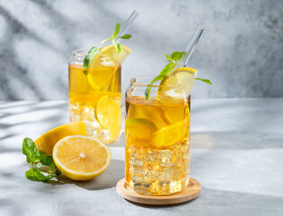 Two glasses with iced drink with lemon and mint on a light background with shadows