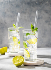 Two glasses mojito cocktail with fresh lime, mint and ice on light background with shadow.