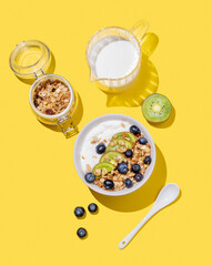 Natural yogurt with granola, kiwi and blueberries in a bowl on a bright yellow background
