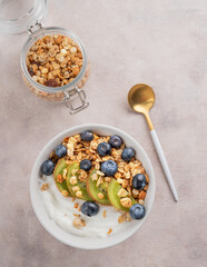 Natural yogurt with granola, kiwi and blueberries in a bowl on a light background with spoon