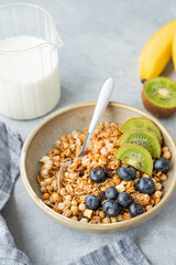  Homemade baked granola or muesli in a bowl with kiwi and blueberries on a light background