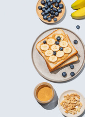 Peanut butter toast on a plate with banana, blueberry and nuts on a blue background.