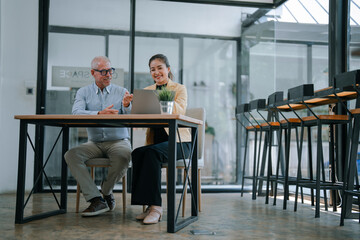 Senior manager and young businesswoman sitting at desk and using laptop together, discussing business strategy and sharing ideas in modern office workplace