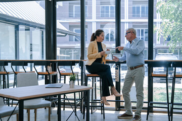 Two businesspeople discussing during a coffee break in a modern office cafeteria, enjoying a cup of...