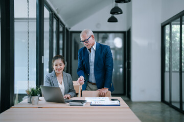 Senior manager pointing at laptop screen coaching young businesswoman working together discussing graphs and charts in modern office. Teamwork. Collaboration. Mentorship. Leadership. Business strategy