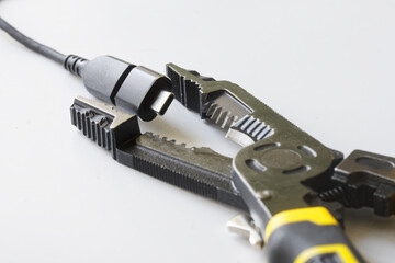Macro shot of USB Type-C connector gripped by multi-tool pliers on white background; ideal for illustrating electronic repair, DIY projects, and device maintenance. Photo
