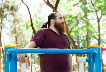 Obraz premium Plus-size man exercising outdoors: stretching, using resistance bands and public gym equipment with confidence and joy in spring weather