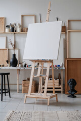 studio featuring a wooden easel with a blank white canvas at the center, surrounded by various art supplies and decorative objects