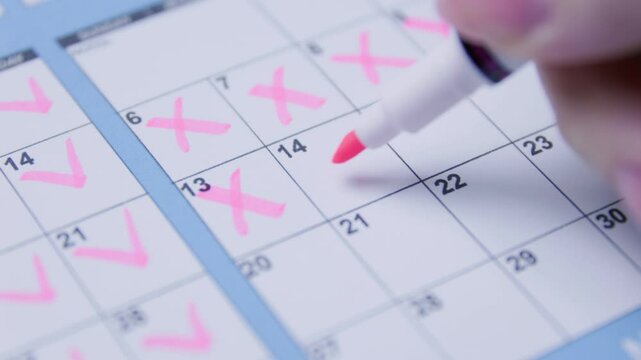 Hand marking pink checkmarks on a calendar, representing planning and tracking.