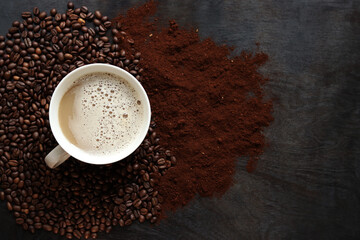 Cappuccino, top view. Cup of cappuccino among coffee beans and ground coffee. Cup of aromatic coffee among roasted coffee beans. Invigorating drink. Copy space