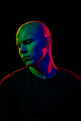 Portrait of handsome young guy with bald head in dark clothes, looking aside, posing with serious...