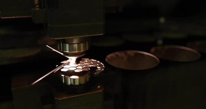 Industrial laser cutting machine processes metal part in workshop at darkness. Machine generates sparks demonstrating precision in modern factory