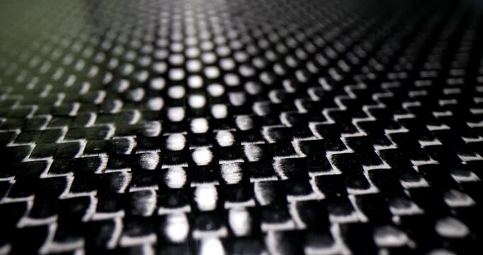 Carbon fiber surface features repeating geometric pattern at bright light. Modern material with strength and lightweight qualities for technology