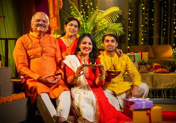 Smiling Indian family greets on Diwali while sitting together indoors with rangoli and decorations
