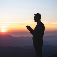 Silhouette of a Man Praying on a Mountain During Sunset With Vibrant Colors in the Sky