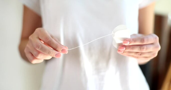 Woman wearing white t-shirt gently opens small container and pulls out light string. Female person prepares to use dental floss for oral hygiene