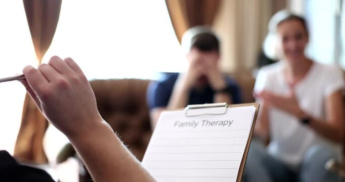 Psychologist writes notes while listening to married couple discussing interpersonal dynamics. Work through emotional tensions during therapy session