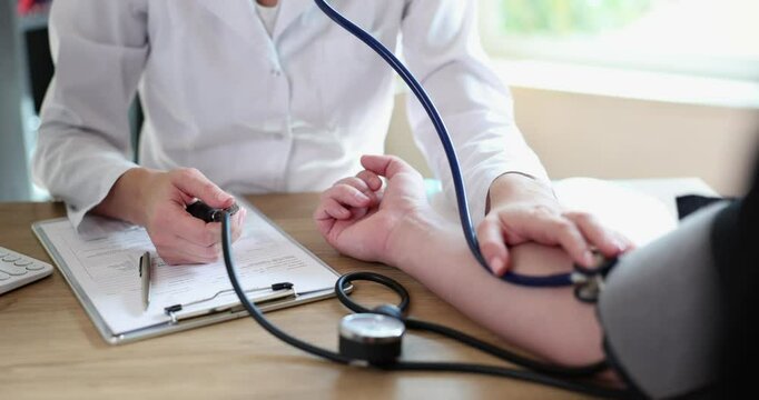 Lady doctor uses sphygmomanometer and stethoscope taking blood pressure measurement of patient at appointment. Medical examination in modern clinic