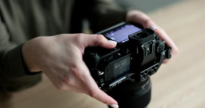 Photographer adjusts camera settings on professional digital single lens reflex camera. Woman utilizes external monitor holding device for stability
