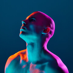 Portrait of young bald man, shirtless, looking upwards, posing shirtless on dark blue background in...