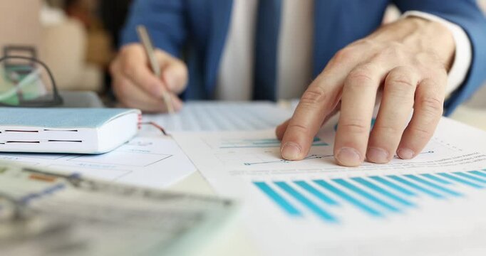 Businessman analyzes financial charts making investment decisions in office. Specialist compares various factors and important data at workplace - Powered by Adobe