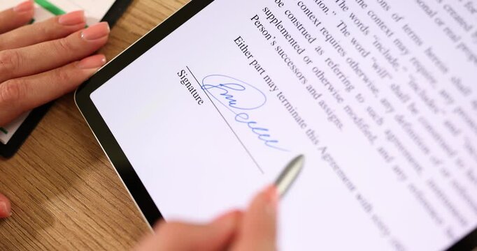 Businesswoman signs digital contract on tablet with stylus pen near paper document with charts and graphs. Electronic signature and paperless office