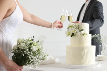 Married couple clinking glasses of champagne at table with wedding cake indoors, closeup