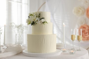 Delicious wedding cake with floral decor and glasses of champagne on table indoors
