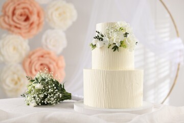 Delicious wedding cake with floral decor and bouquet on table indoors