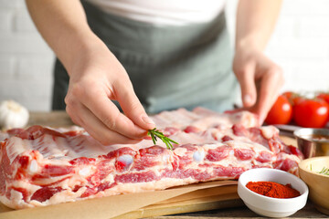 Woman putting rosemary onto raw pork ribs at table, closeup