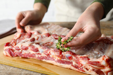 Woman putting thyme onto raw pork ribs at table, closeup