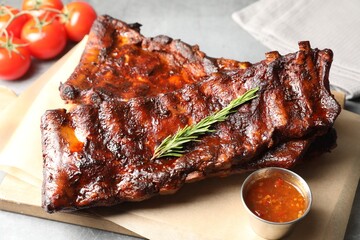 Tasty roasted pork ribs served with rosemary, tomatoes and sauce on light grey table, closeup