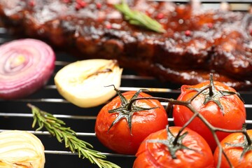 Delicious roasted pork ribs with rosemary, onions and tomatoes on grill, closeup