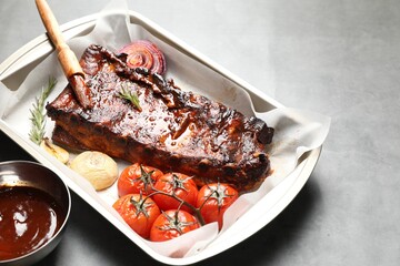 Delicious spare ribs, baked onion, sun dried tomatoes and sauce on grey table, closeup