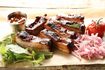 Delicious pork ribs, sauce, arugula and onion on wooden table, closeup