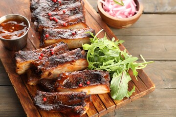 Delicious pork ribs, arugula, sauce and onion on wooden table, closeup