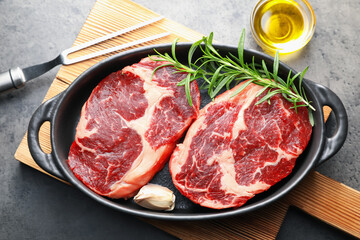 Pieces of raw beef meat with spices in baking dish, oil and fork on gray textured table, flat lay