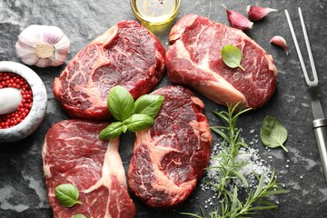 Pieces of raw beef meat, spices and carving fork on dark table, flat lay