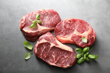 Pieces of raw beef meat and basil on grey table, flat lay