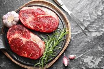 Pieces of raw beef meat, spices and carving fork on dark table, flat lay. Space for text