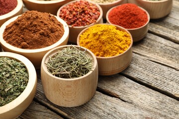 Different aromatic spices in bowls on wooden table, closeup. Space for text