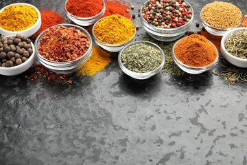 Different aromatic spices in bowls on dark table, above view. Space for text