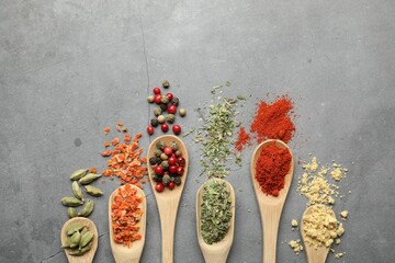 Many different spices in spoons on grey table, flat lay. Space for text