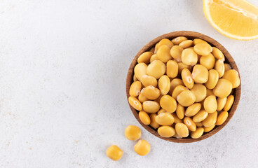 Pickled lupini beans in a wooden plate with lemon on a gray background. Top view. Copy space. Plant protein.